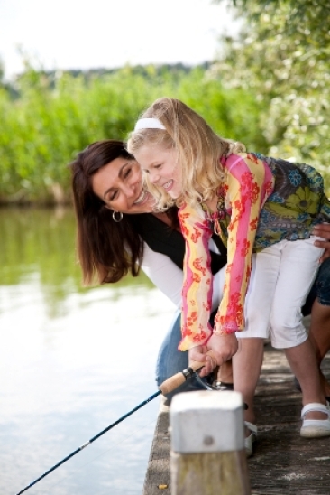 Cute young girl trying to catch a fish with mom watching over her